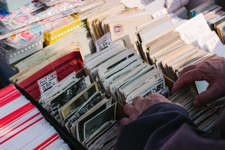 Image of an older man's hands as he flips through a box of vintage postcards