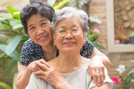a mother and daughter smiling at the camera. The mother is in front and the daughter has her arms around her