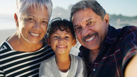 An older Latinx couple with their granddaughter. All three smiling at the camera