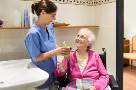 Care worker handing an older woman her toothbrush. Both are smiling.