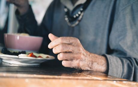 closeup of an older man's hand next to his plate of food