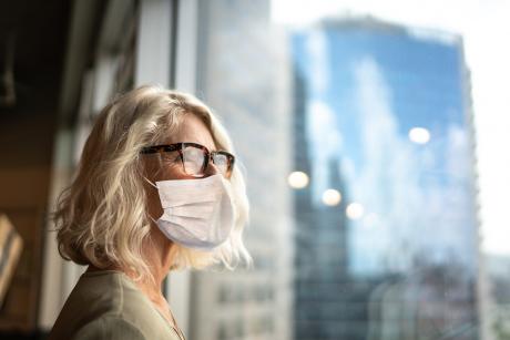 Mature professional woman looking out of window with face mask