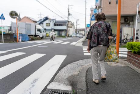Elder walking alone away from camera on sidewalk