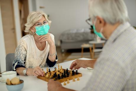 An older woman and man play chess, wearing masks