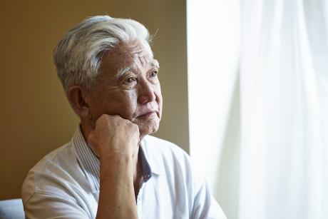 older man looks out window, seems sad or contemplative