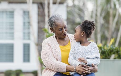 A 4 year old African-American girl sitting on her great grandmother's lap outside her house. 