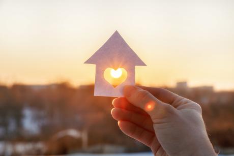 House of paper with a heart held over the rising sun background.