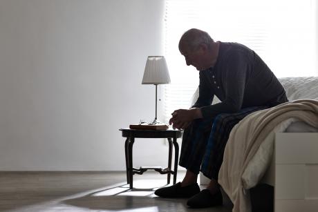 Older man sitting on bed looking serious