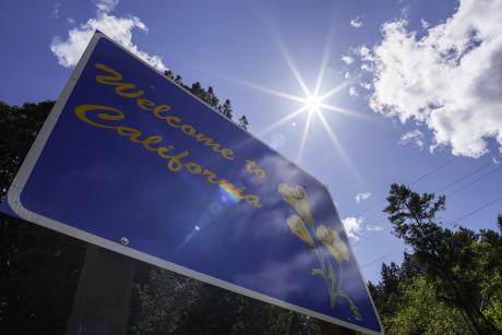 Blue sign that says "Welcome to California" in front of sunny sky
