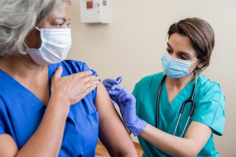 A nurse giving a care worker a shot