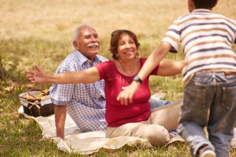 grandson runs toward grandparents, sitting on picnic blanket in the park