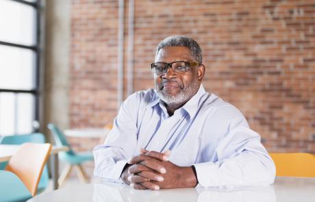 Older man sitting at table, hands folded, looing at the camera