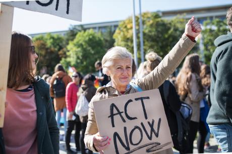 Person at protest holding sign that reads "Act Now"