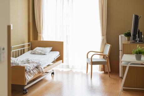 Empty nursing home room with unmade bed, chair window tray table, dresser