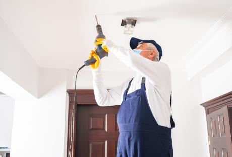 An older man wearing a face mask doing home repairs