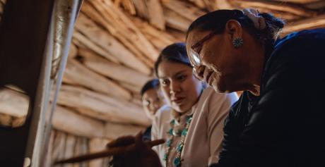 An elder Indian woman teaching younger people to weave