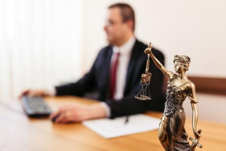 Justice status in focus with a lawyer working at his desk blurred in the background
