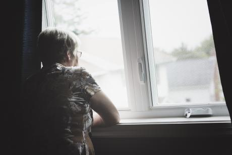 An older woman looks out the window
