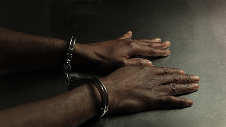 Black man's hands in handcuffs on table