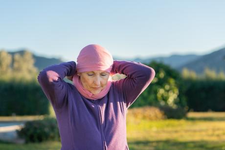 older woman ties on pink scarf/cancer