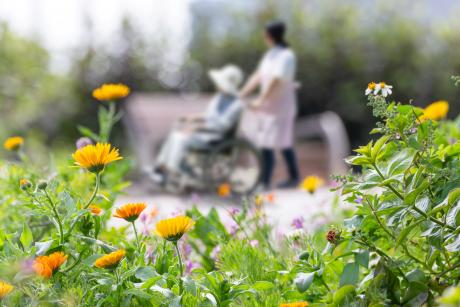 A caregiver walks an older woman through a park